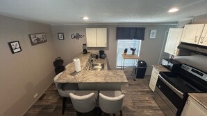 A compact kitchen with a central island, bar stools, a coffee station, and a stove.