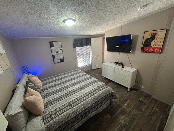 A bedroom with a bed, a dresser, a TV, and a poster on the wall.