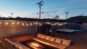 Ein Außenbereich mit Terrasse, Feuerstelle, einer Couch und einem Whirlpool.