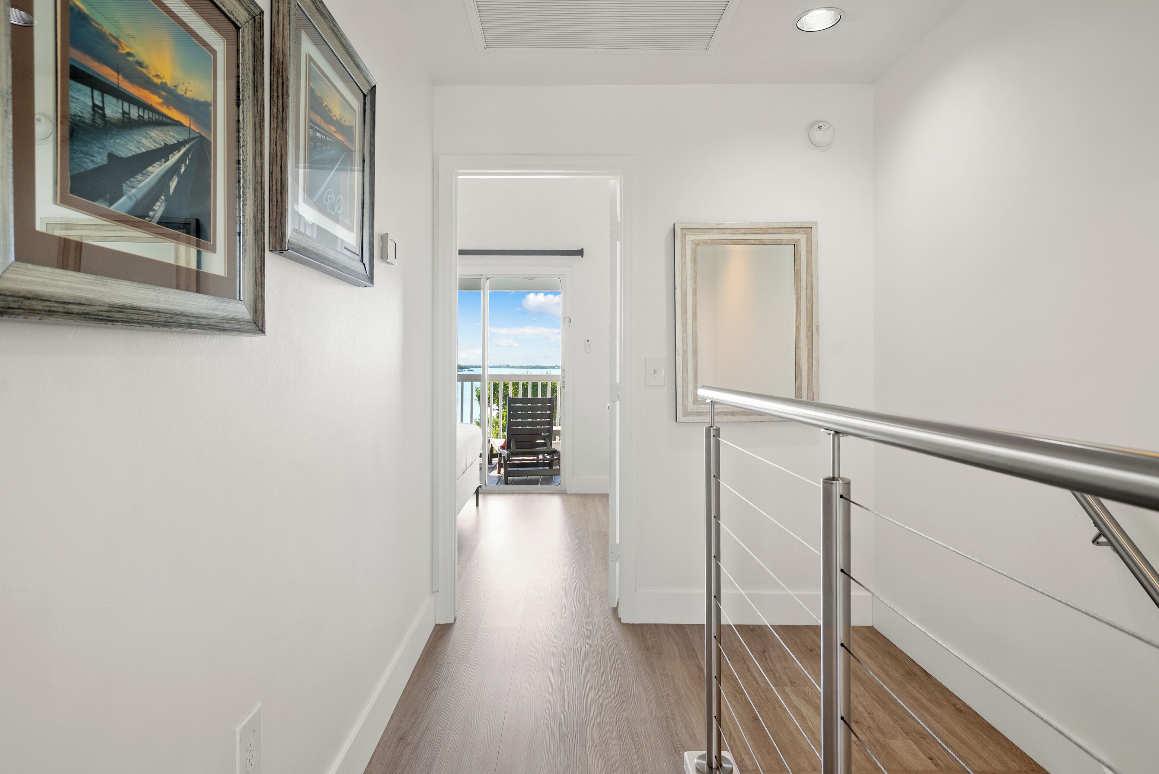 A hallway with wooden flooring, a metal railing, and framed artwork on the walls.