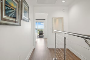 A hallway with wooden flooring, a metal railing, and framed artwork on the walls.