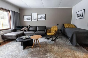 A modern living room with a sectional sofa, a rocking chair, a small round table, and a bed with a headboard. - Cozy Koivutie Apartment (Ranua)