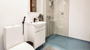 A modern bathroom with a toilet, sink, and glass shower enclosure. - Cozy Koivutie Apartment (Ranua)