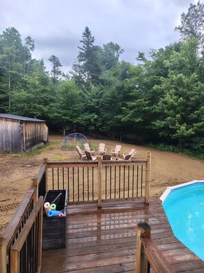 A wooden deck with a pool, surrounded by trees and a sandy area. - Country house with a forest trail and a mountain bike trail nearby. (Mandeville)
