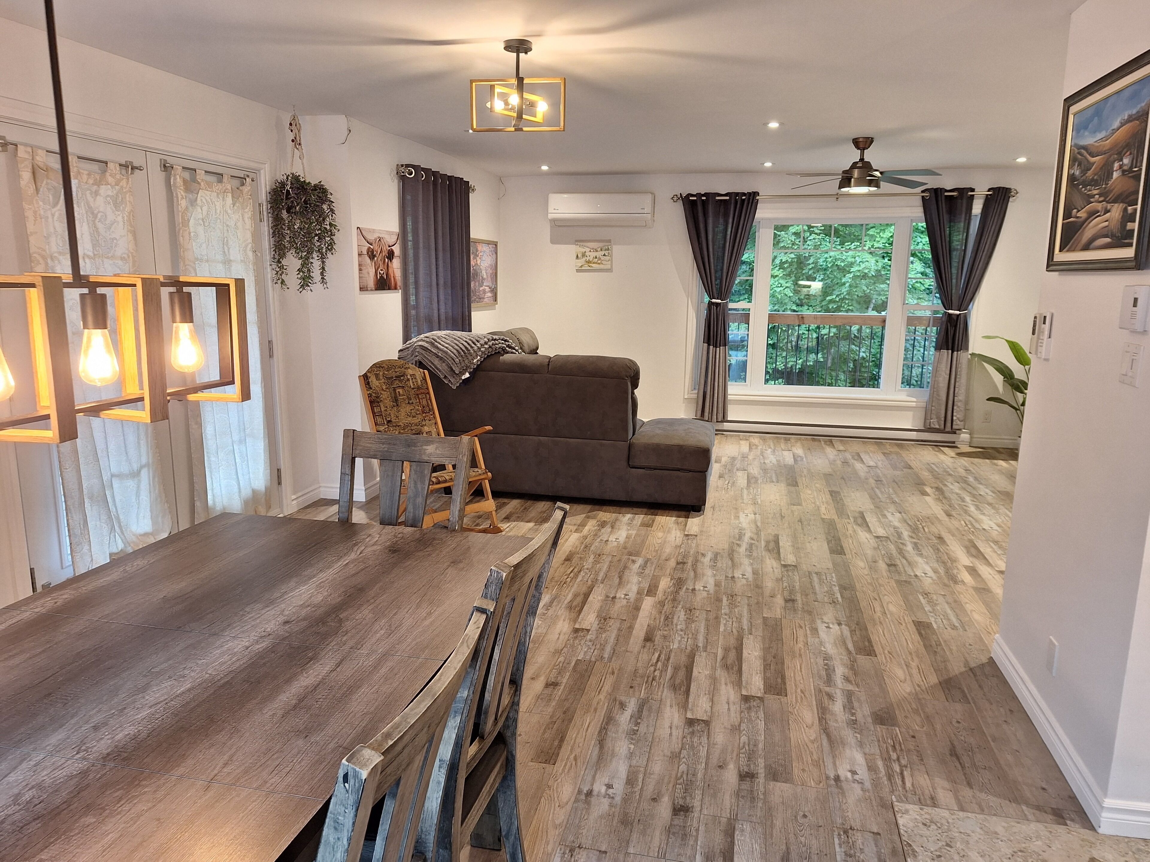 Een moderne woonkamer met een houten eettafel, een bruine bank en een plafondventilator.