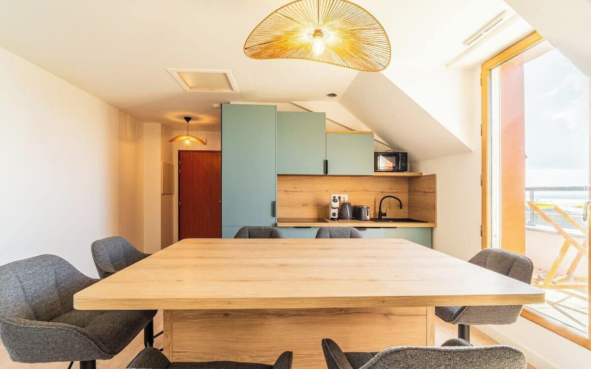 Una cocina moderna con una mesa y sillas de madera, un lámpara colgante y vistas al exterior.