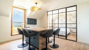 A modern kitchen with a wooden countertop, black bar stools, and a large window offering a view of the sea.