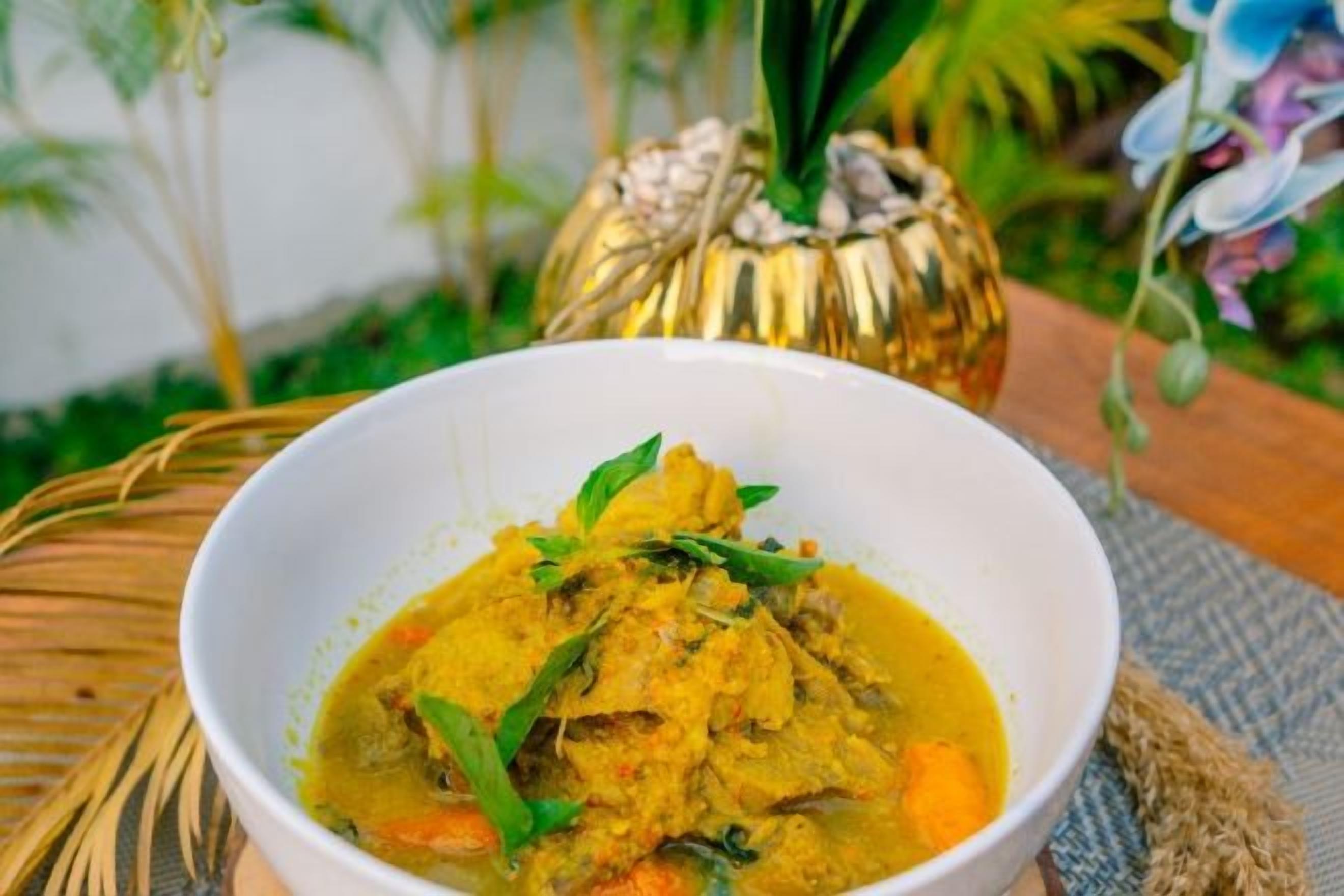 Un tazón de curry con verduras y hierbas, sobre una estera tejida.