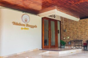 L’entrée d’un hôtel, avec une enseigne indiquant « Niklem Singgah » et un plafond en bois.