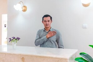 Una persona de pie en la recepción, con una planta a la izquierda.