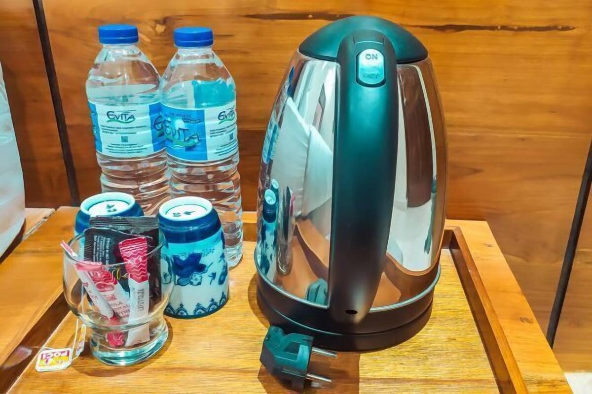 Een waterkoker, twee waterflessen en een glazen pot met theezakjes op een houten oppervlak.