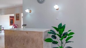 Un área de recepción con mostrador de mármol, un reloj y luminarias fijadas a la pared.