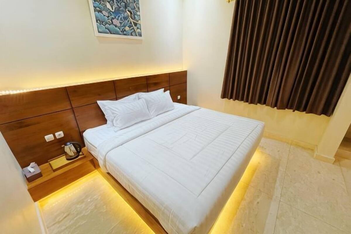 Een hotelkamer met een groot bed, een houten hoofdeinde, nachtkastjes en een schilderij aan de muur.