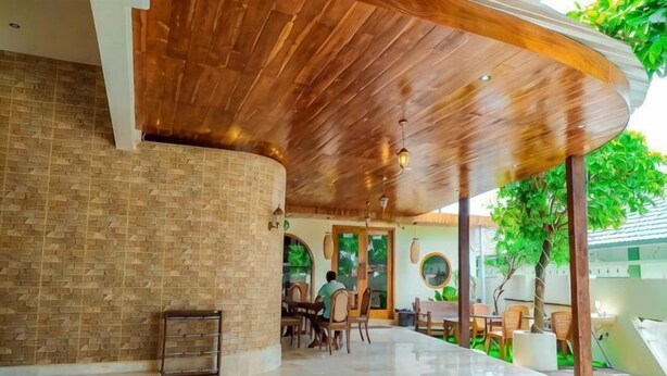 Un amplio espacio interior con techo de madera curvada, pared de ladrillo y zona de estar con mesas y sillas.