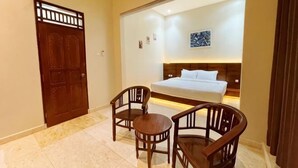Habitación de hotel con cama, dos sillas de madera, una mesita, una puerta y una obra de arte colgada en la pared.