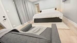 Un dormitorio moderno con una cama, un sofá gris y un televisor de pantalla plana en la pared.