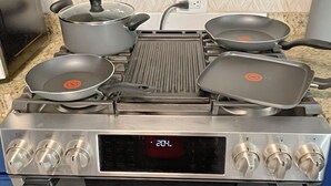 Una cocina con estufa de acero inoxidable, cuatro sartenes, una olla y una pantalla digital.