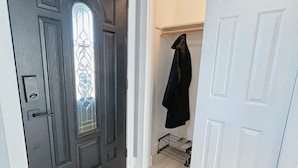 Un pasillo con una puerta negra que incluye un vitral, una puerta blanca y un felpudo con la inscripción 