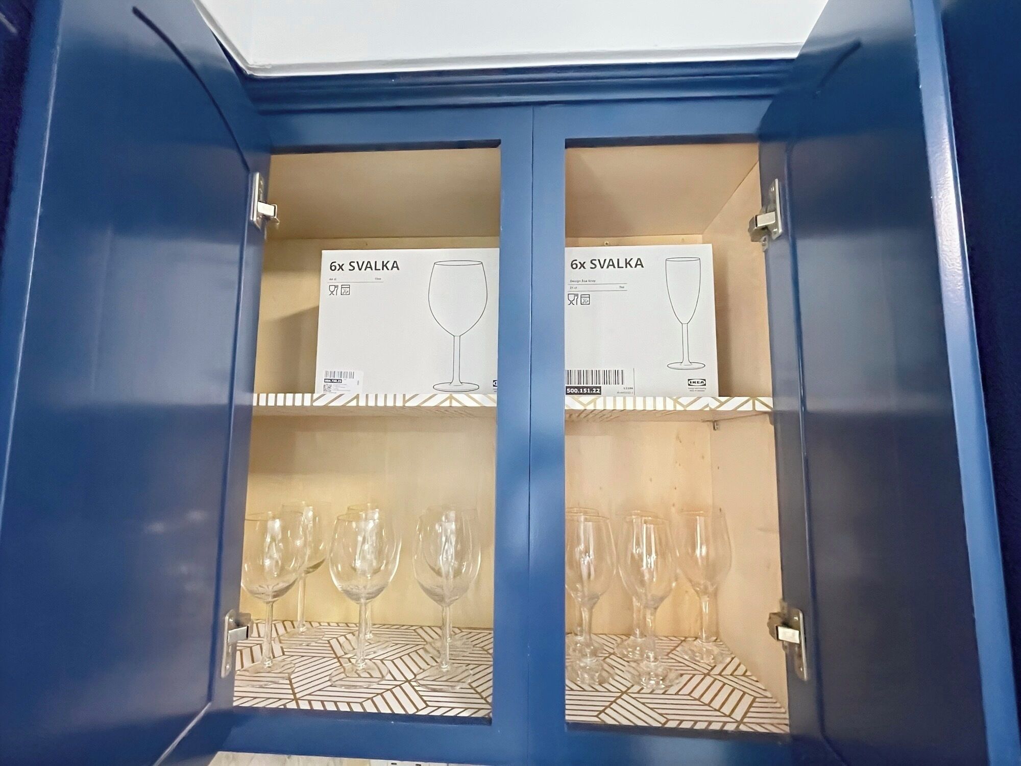 A blue cabinet with two shelves, each containing a box labeled '6x SVALKA' and a pair of wine glasses.