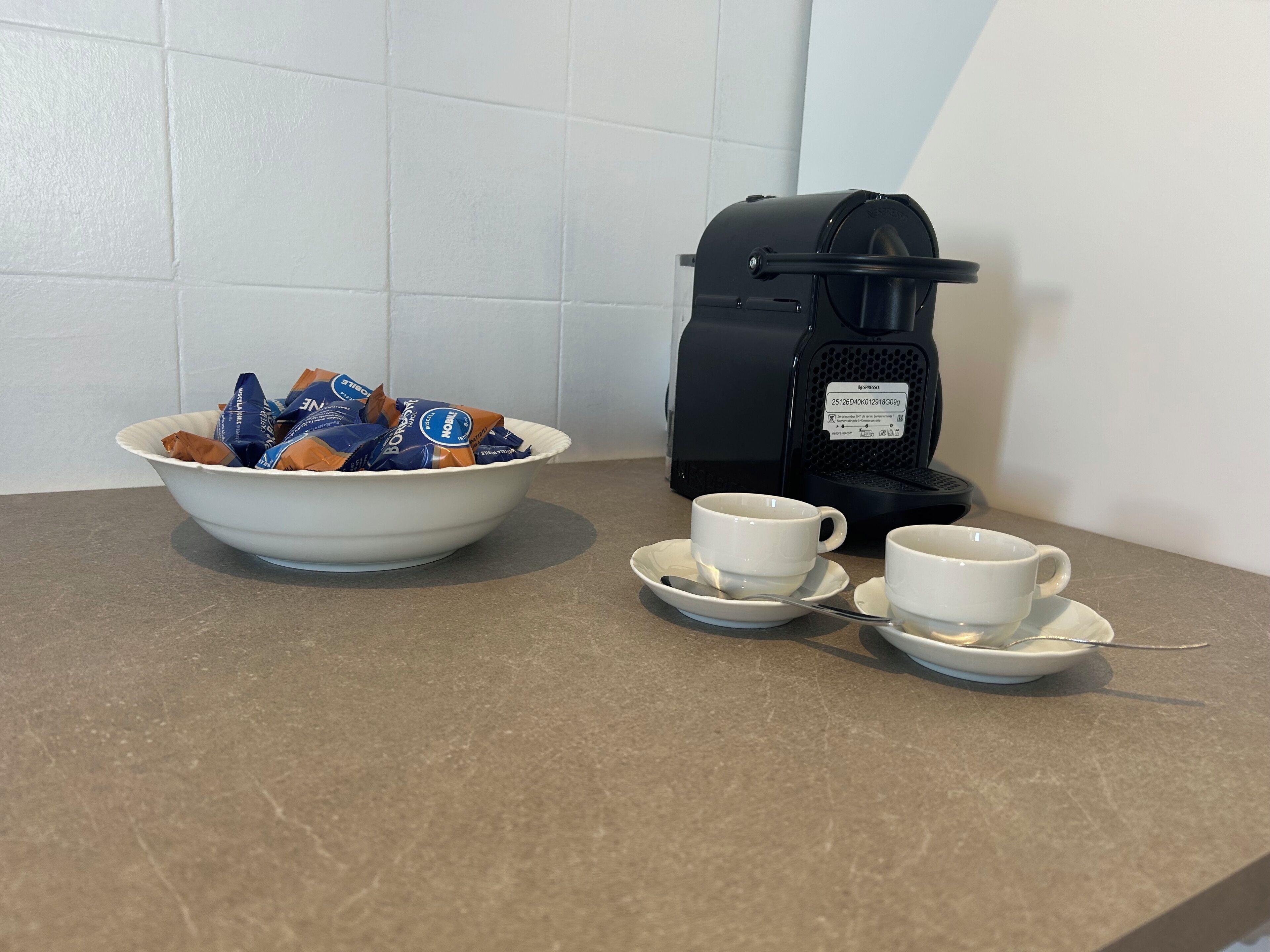 Una cafetera, un tazón de cápsulas de café y dos tazas sobre una encimera.
