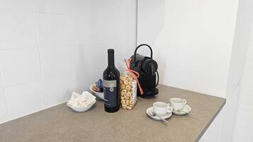 Un plan de travail de cuisine avec une bouteille de vin, un paquet de biscuits, une machine à café et deux tasses posées sur un comptoir de couleur beige.
