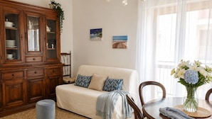 A living room with a sofa, a wooden cabinet, a dining table with chairs, and artwork on the wall. - Dimora Peppino, a family friendly holiday home, just few step from the sea. (Polignano a Mare)