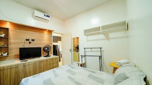 A bedroom with a bed, a TV, a fan, a wardrobe, and a small table with a towel.