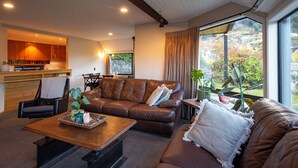 A modern living room with a brown leather sofa, a wooden coffee table, and a dining area with wooden cabinets and a stone wall.