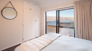A bedroom with a bed, a wardrobe, and a view of a balcony with a mountain backdrop.