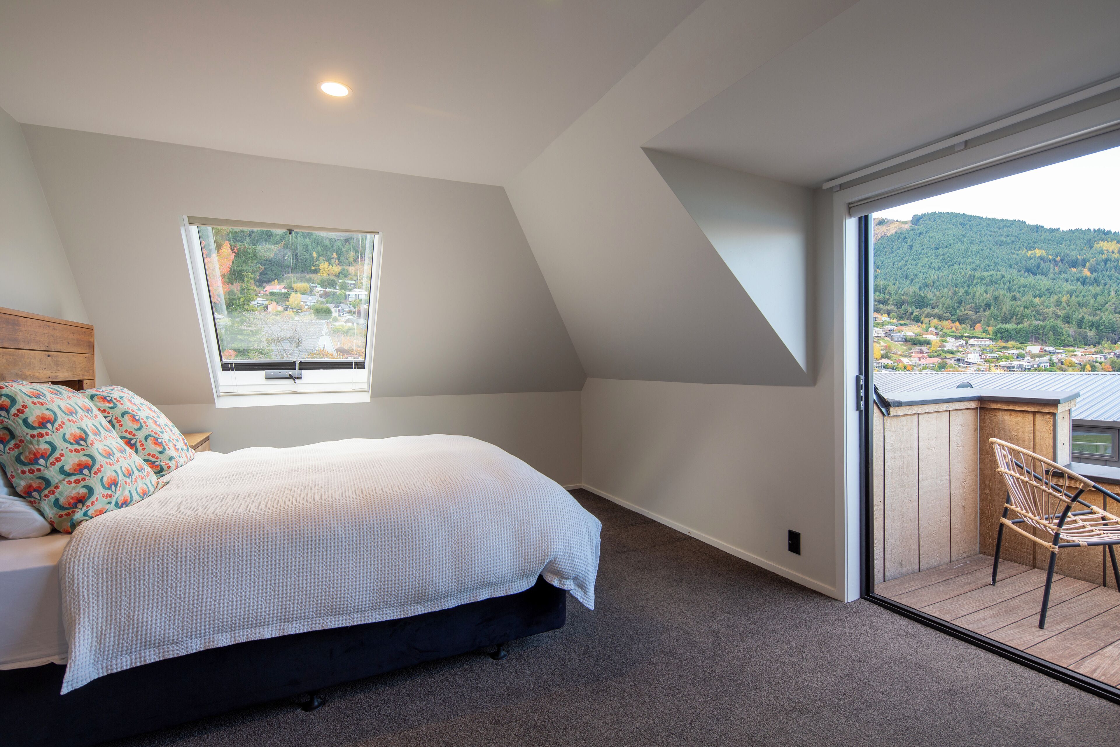A bedroom with a bed, a window, and a balcony with a view of a town and hills.