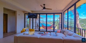 A spacious living room with a large sofa, a yellow armchair, and a ceiling fan. A large window offers a view of a mountainous landscape. - PISCIS CONDO
Dawn overlooking the most beautiful bay in Mexico. (Zihuatanejo)