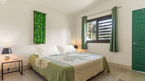 Un dormitorio con una cama, una mesita de noche, una lámpara, una ventana con cortinas y una puerta verde.