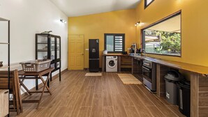 Cocina compacta con lavadora, cafetera y ventana con vista a la vegetación.