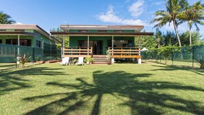 Una casa de dos pisos con un porche cubierto, patio cercado y palmeras.