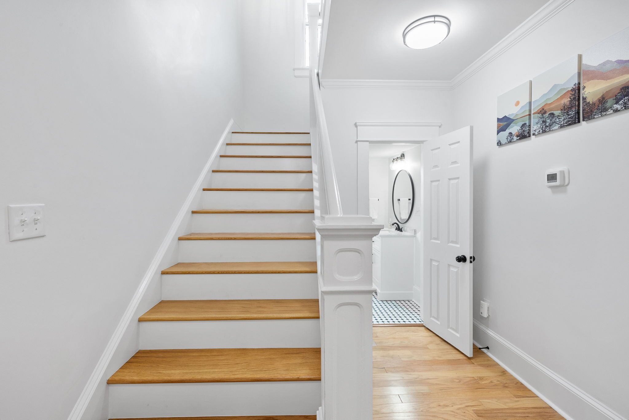 A staircase with white walls and wooden steps leading to a door with a light fixture above.