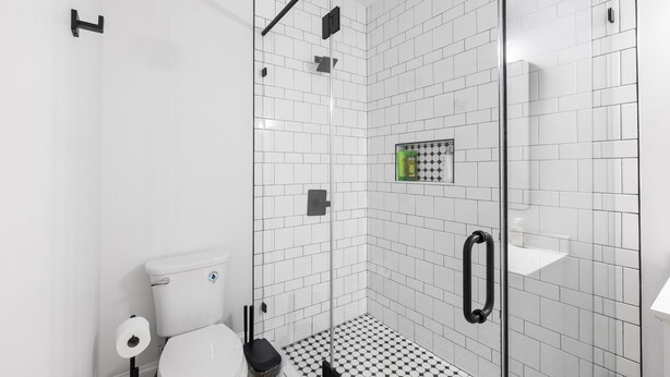 Un baño moderno con cabina de ducha de vidrio, paredes de azulejos blancos y un suelo con estampado de cuadros.