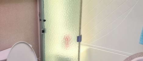 Une salle de bain comprenant des toilettes, une douche avec des portes en verre dépoli et un lavabo avec un plan de travail à motifs.