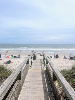 A wooden boardwalk leading to a sandy beach with umbrellas and beach chairs.
