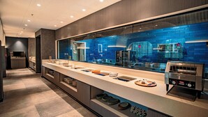 A modern kitchen with a long counter, a toaster, and a view of the city through a large window. - Welina Hotel  (Bhubaneshwar)