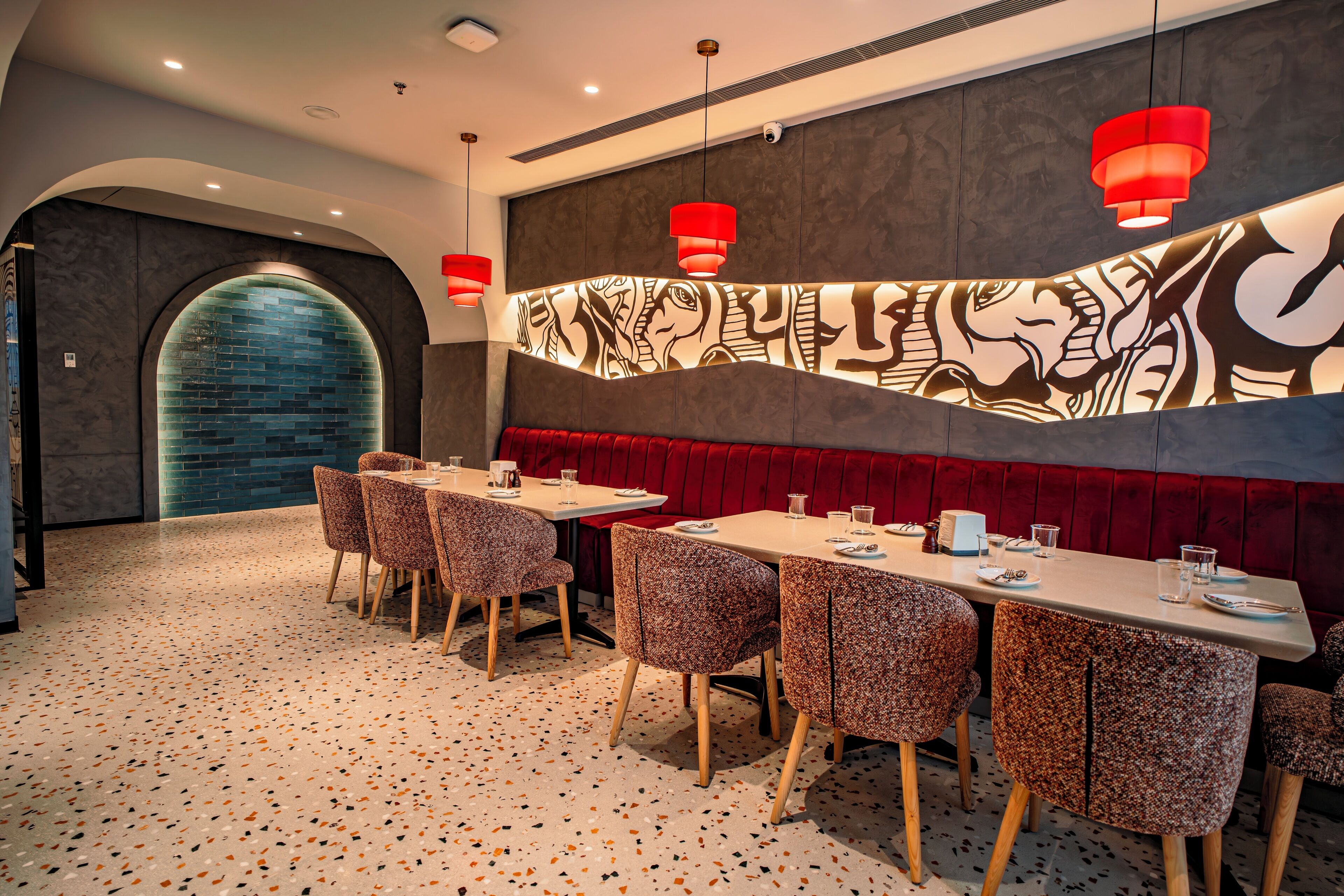 Un restaurante con una mesa larga, asientos tipo banca acolchados en rojo y sillas con estampado.