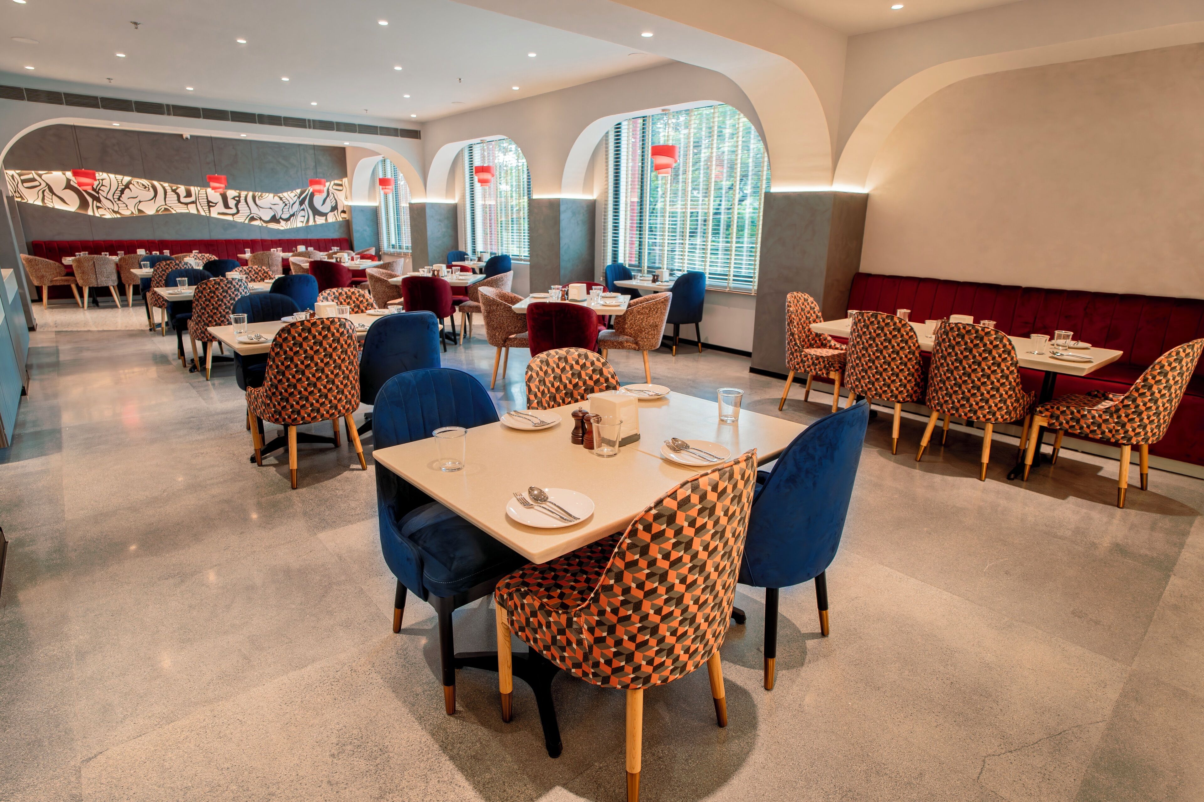 Een restaurant met meerdere eettafels en stoelen, met een mix van gestreept en effen gestoffeerde zitplaatsen.