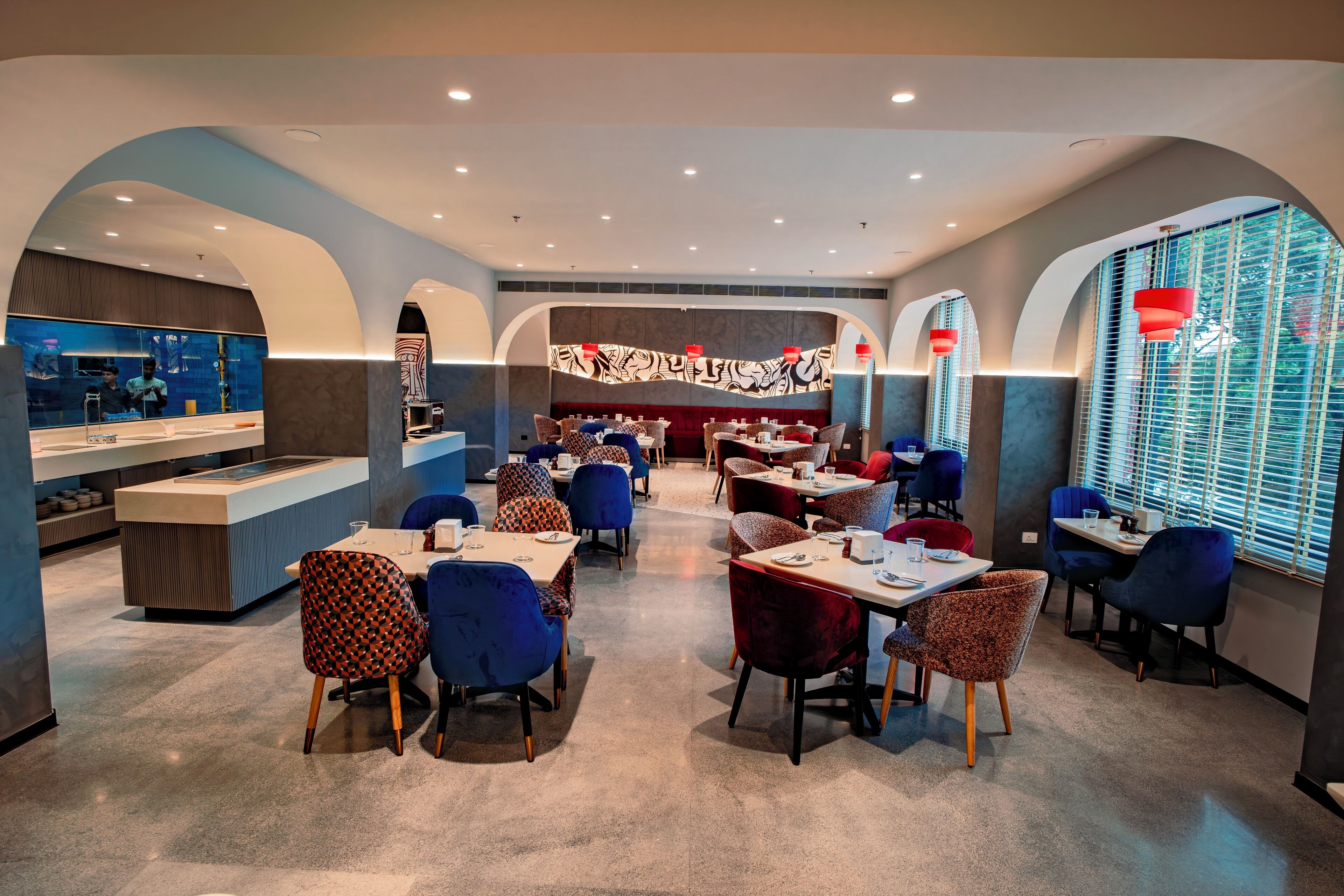 Un restaurant moderne doté d’un bar central, de nombreuses tables et de chaises aux couleurs vives.