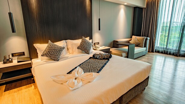 A modern hotel room with a large bed, a sitting area, and a view of the outdoors. - Welina Hotel  (Bhubaneshwar)