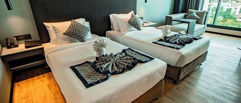 A modern hotel room with two beds, a sofa, a nightstand, and a large window offering a city view.