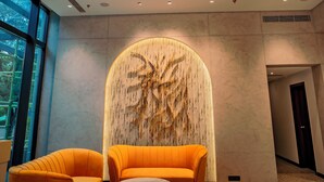 A modern lobby with a curved wall, two orange sofas, a coffee table, and a patterned rug. - Welina Hotel  (Bhubaneshwar)