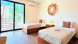 A hotel room with two beds, a large window with a view of trees, a wall-mounted air conditioner, and a woven wall decoration.