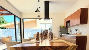 A modern kitchen with wooden cabinets, a large island, and a dining area with chairs and a table.