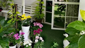 A small garden area with various potted plants and flowers, a white bench, and a window with a view of a green lawn. - Ella Way Resort-Kandy (Hindagala)
