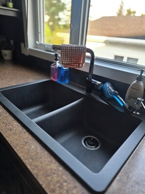 A kitchen sink with a window above it, a soap dispenser, and a bottle of hand soap. - ○Small Town Pearl○ 2Level Hidden Gem Near RedDeer│1K+2Q│Private Yard│Firepit+BBQ (Penhold)