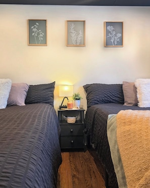 Un dormitorio con dos camas, una mesita de noche con una lámpara y tres láminas botánicas enmarcadas en la pared.